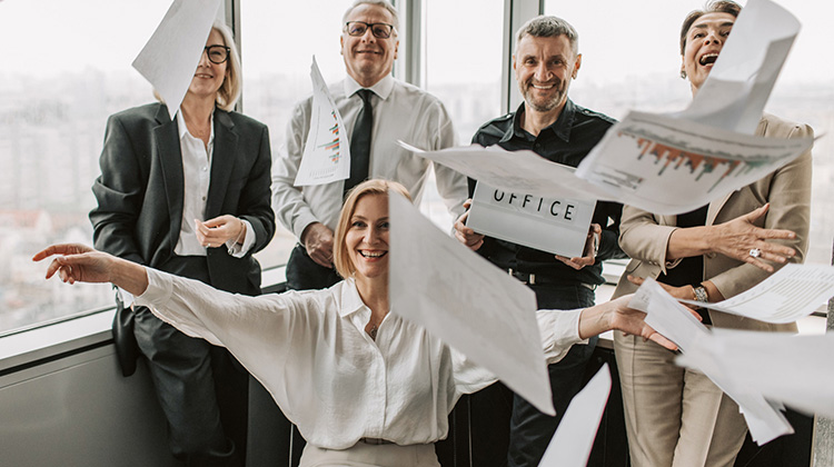 Imagen de una sala de juntas con gente vestida formalmente. Todos están contentos, sonriendo, en una actitud como de liberación. En la imagen hay varios documentos sueltos en el aire, como si un segundo antes los hubiesen aventado a propósito.