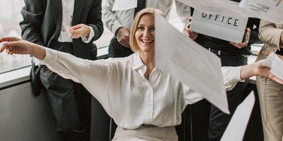 Imagen de una sala de juntas con gente vestida formalmente. Todos están contentos, sonriendo, en una actitud como de liberación. En la imagen hay varios documentos sueltos en el aire, como si un segundo antes los hubiesen aventado a propósito.